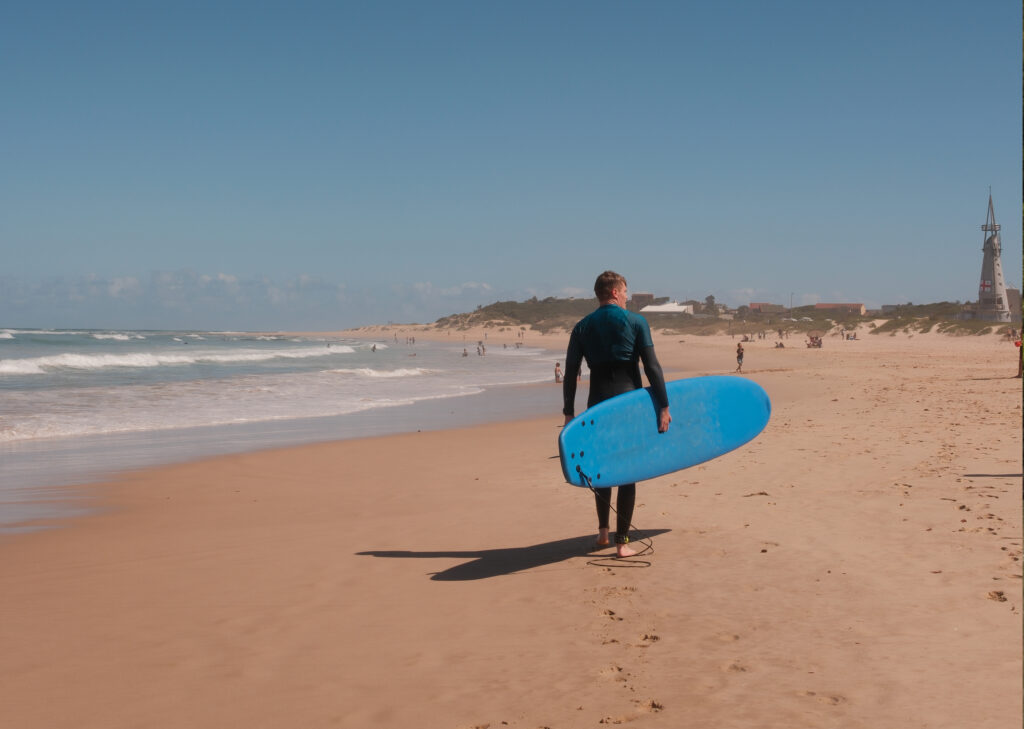 Surfer met een blauwe surfplank op het strand van Jeffreys Bay