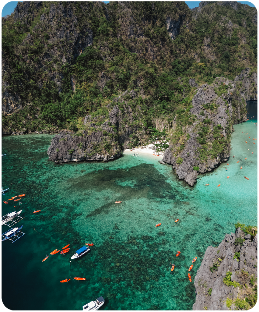 Luchtfoto van de Big Lagoon in El Nido, Filipijnen met oranje kajaks, bangka boten en helder turkoois water tussen kalkstenen rotswanden
