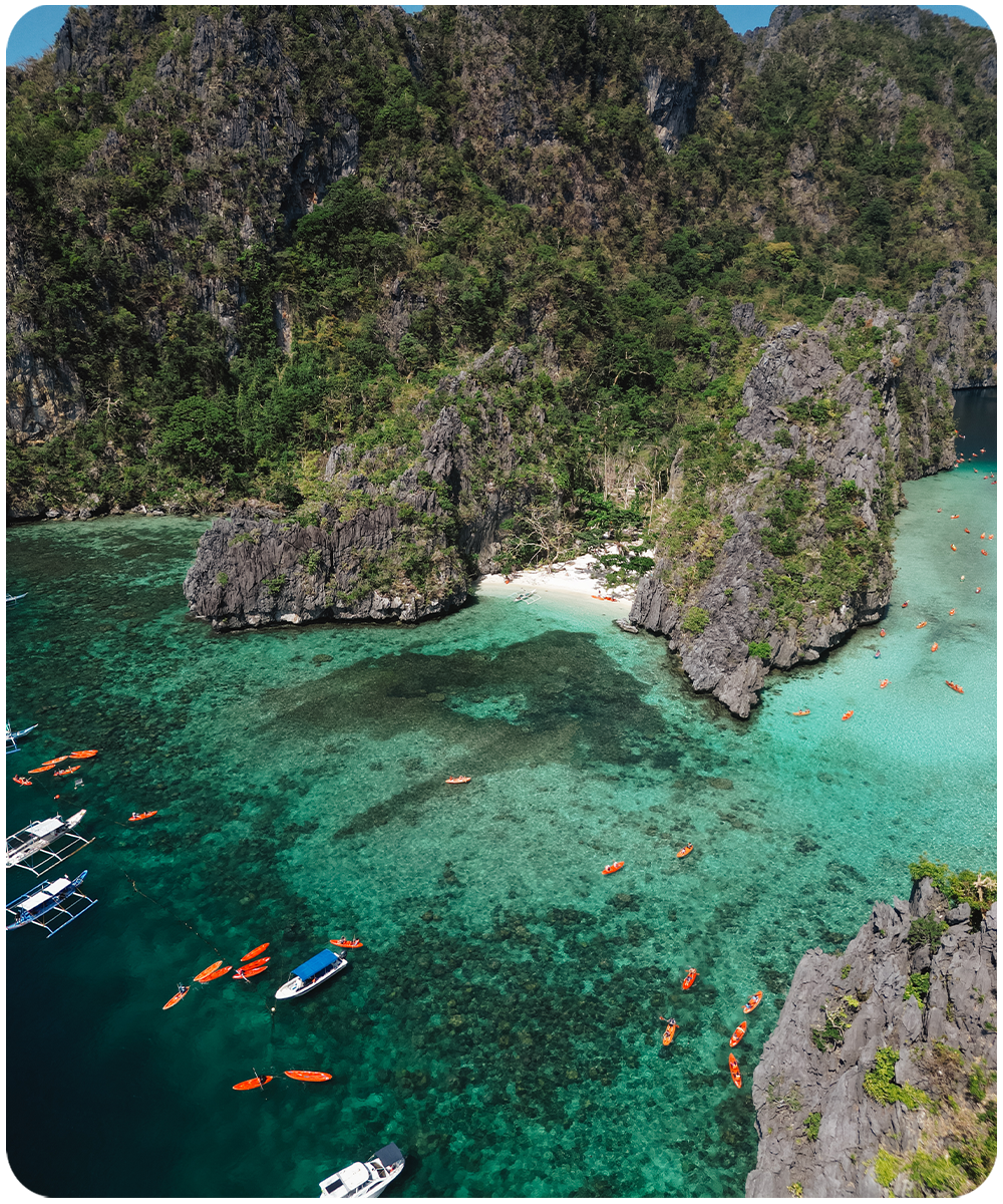 Luchtfoto van de Big Lagoon in El Nido, Filipijnen met oranje kajaks, bangka boten en helder turkoois water tussen kalkstenen rotswanden