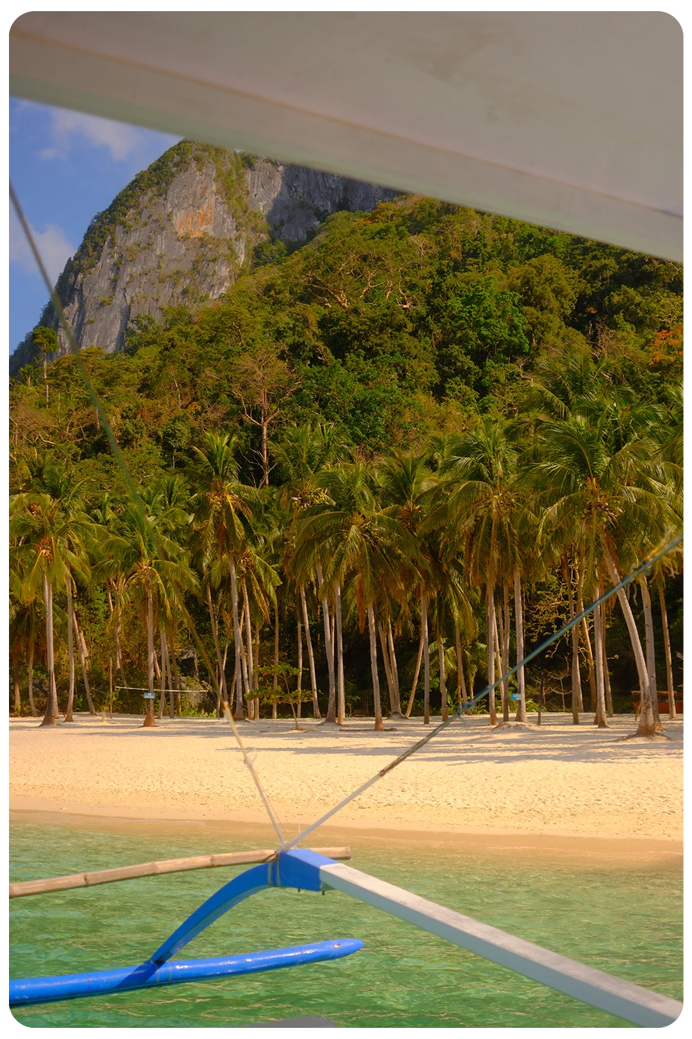 Uitzicht vanuit een traditionele bangka boot op een wit strand met palmbomen en kalkstenen rotsen in El Nido, Filipijnen