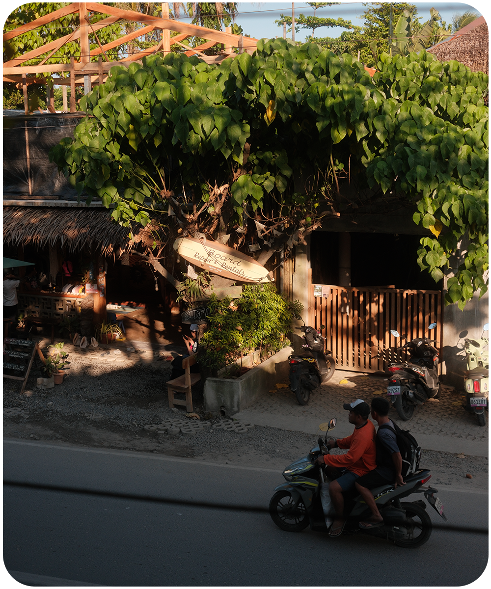 Lokale straat in General Luna op Siargao met scooters, tropische bomen en gezellige surf cafés