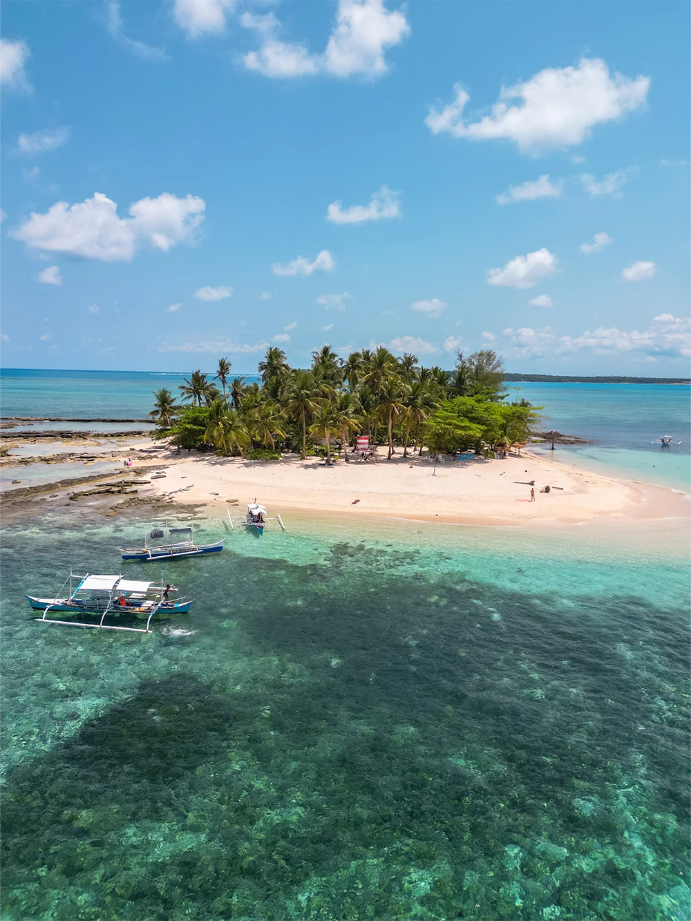Luchtfoto van Guyam Island op Siargao, Filipijnen met een wit strand, palmbomen en twee bangka boten in het heldere turkooise water