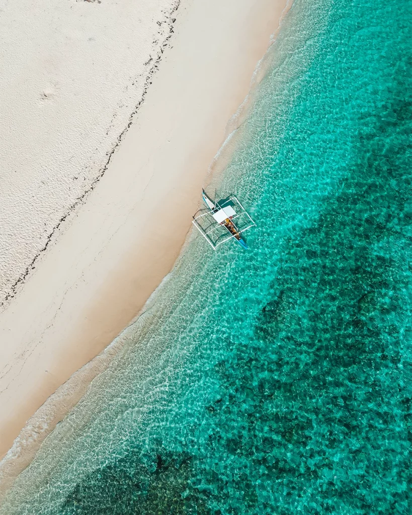 Luchtfoto van een bootje bij een wit strand en turquoise zeewater