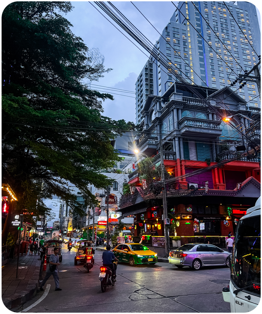 Drukke straat in Bangkok in de avond met tuk tuks, taxi's, neonreclames en hoge gebouwen op de achtergrond