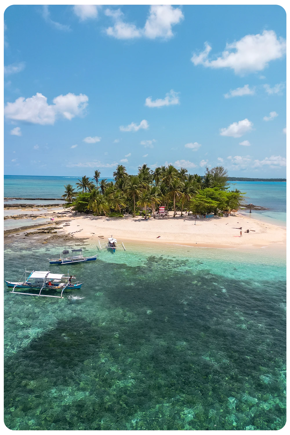 Reisgids Filipijnen Luchtfoto van Guyam Island op Siargao, Filipijnen met een wit strand, palmbomen en twee bangka boten in het heldere turkooise water