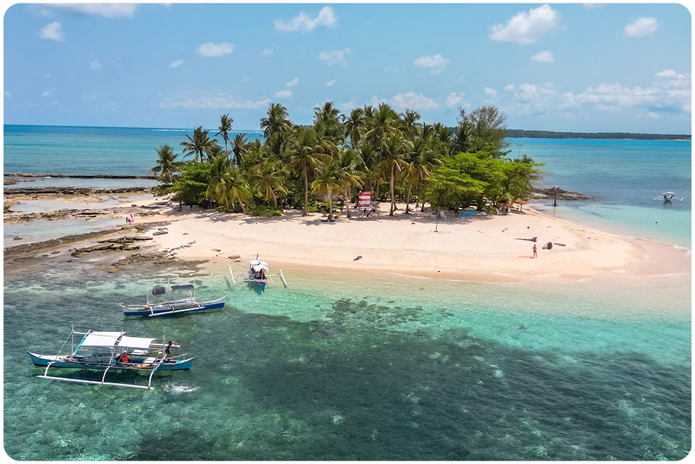 Luchtfoto van Guyam Island op Siargao, Filipijnen met een wit strand, palmbomen en twee bangka boten in het heldere turkooise water