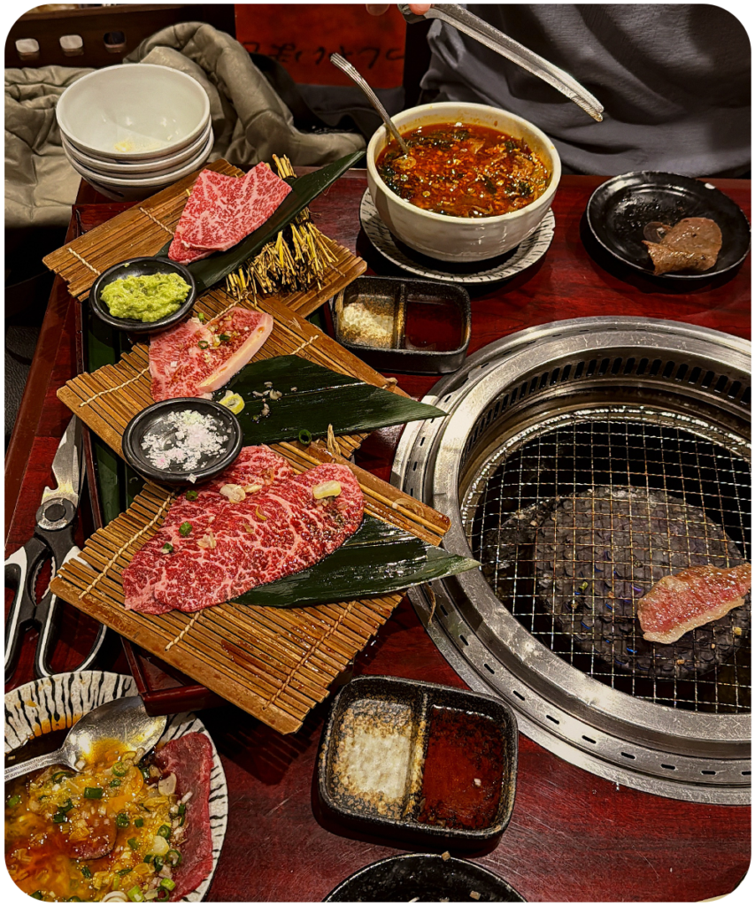 Japanse yakiniku bij Hinomaru met sterk gemarmerd wagyu vlees op een bamboe plateau naast een ingebouwde tafelgrill, geserveerd met wasabi en dipssauzen