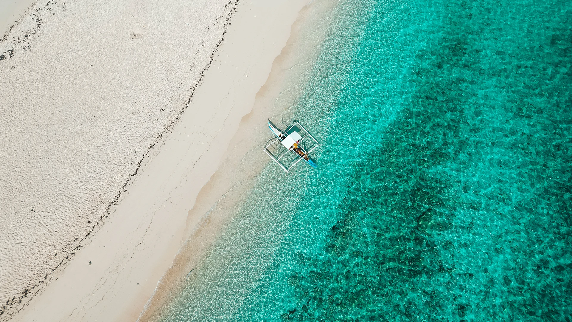 Luchtfoto van een wit strand met een boot in helder zeewater